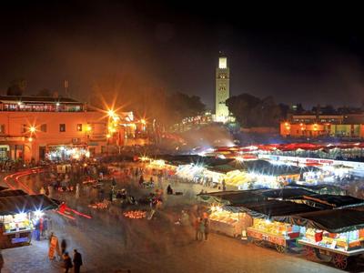 Beleuchteter belebter Markt bei Nacht mit Ständen und Turm im Hintergrund.