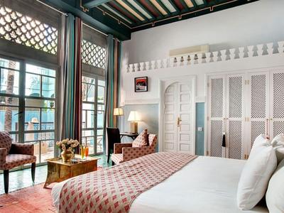 Modern hotelkamer met groot bed, fauteuils en veel natuurlijk licht.