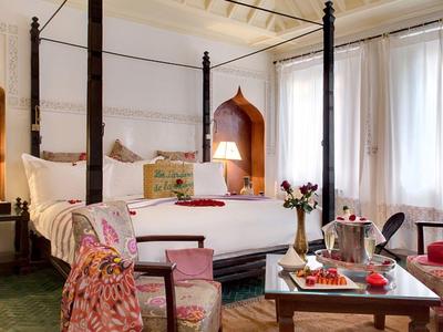 Elegant slaapkamer met hemelbed, fauteuils en groot raam met witte gordijnen.