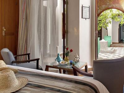 Lichte hotelkamer met twee fauteuils, tafel en uitzicht op een binnenplaats met boog.