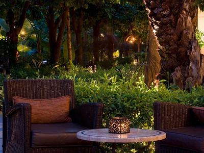 Knusse zithoek met twee stoelen en een tafel, omgeven door een weelderige tuin bij zonsondergang.