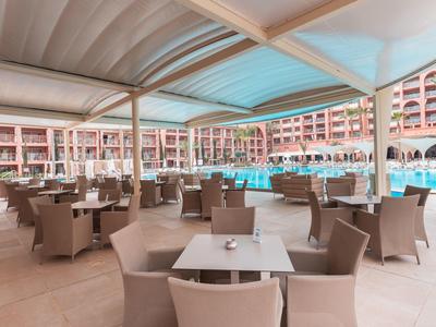 Overdekt buitenterras met tafels en stoelen naast een hotelzwembad.