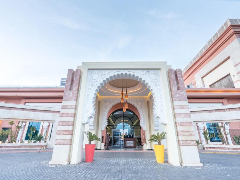 Hotelentree met grote boog, zuilen en twee kleurrijke plantenbakken.