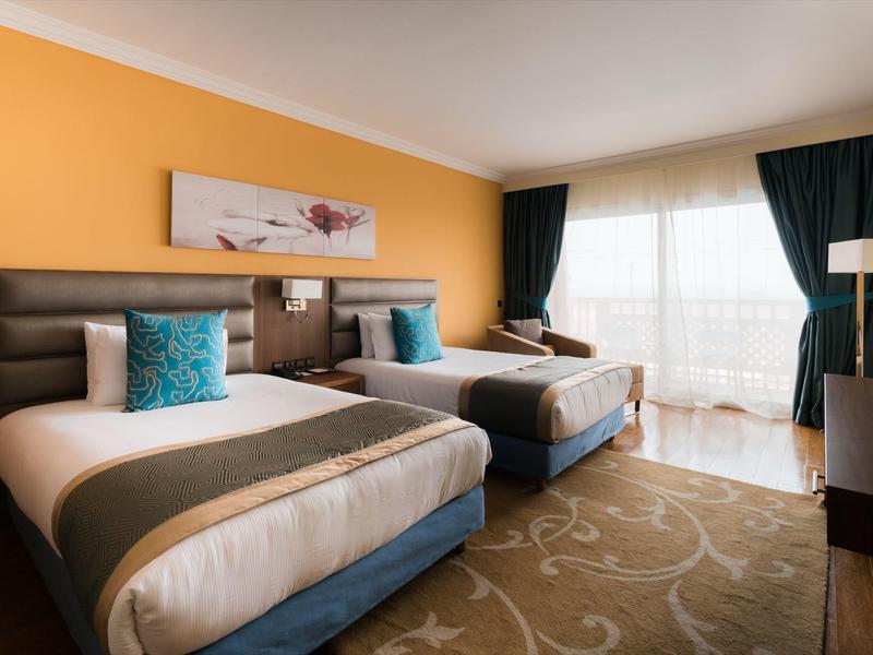 Kamer met twee eenpersoonsbedden, oranje muur, blauwgrijze gordijnen en tapijt.