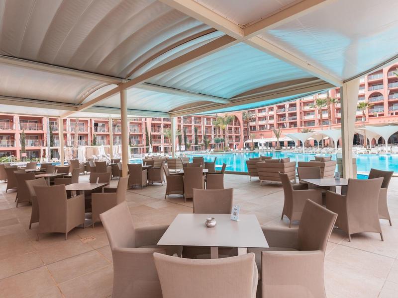 Overdekt buitenterras met tafels en stoelen naast een hotelzwembad.