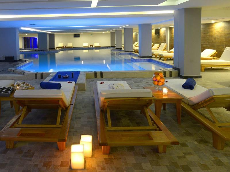 Binnenzwembad in een luxe wellnessruimte met ligstoelen en zachte verlichting.