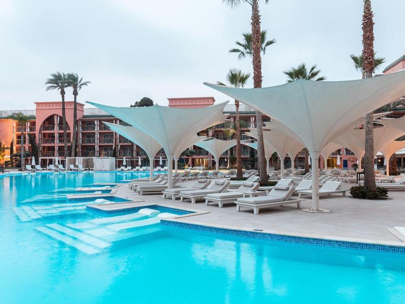 Zwembadgedeelte van resort met witte zonneschermen en ligbedden bij het blauwe water.