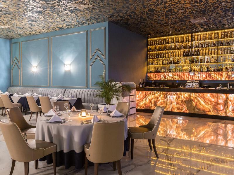 Elegant restaurant met ronde tafels, comfortabele stoelen en verlichte marmeren bar.