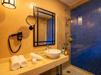 Moderne Badezimmer mit gelber Wand, runder Waschschale, drei weißen Handtüchern und blauem Duschbereich.