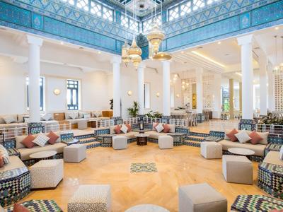 Großer heller Raum mit blauen Decken, weißen Säulen und vielen Sitzgruppen aus grauen Sofas mit bunten Kissen.