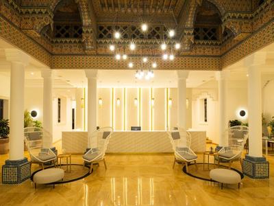 Großer, hell erleuchteter Raum mit beigen Wänden, Säulen, Sesseln und einem glänzenden Boden.