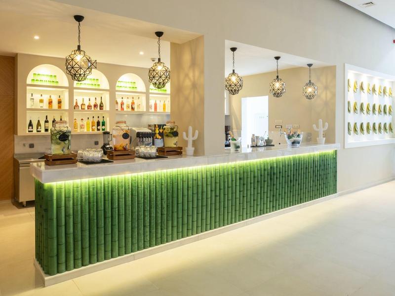 Moderner Barbereich mit grün beleuchtetem Tresen, hängenden Lampen und hellem, minimalistischem Design.