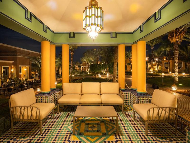 Offener Sitzbereich mit beigen Sofas, gelben Säulen und gemustertem Boden, warm beleuchtet.