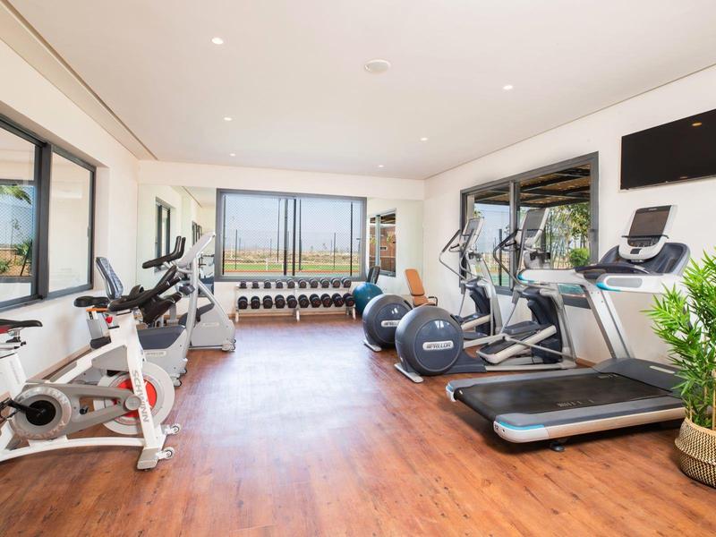 Moderner Fitnessraum mit Laufbändern, Fahrrädern, Gewichten und großen Fenstern für Tageslicht.