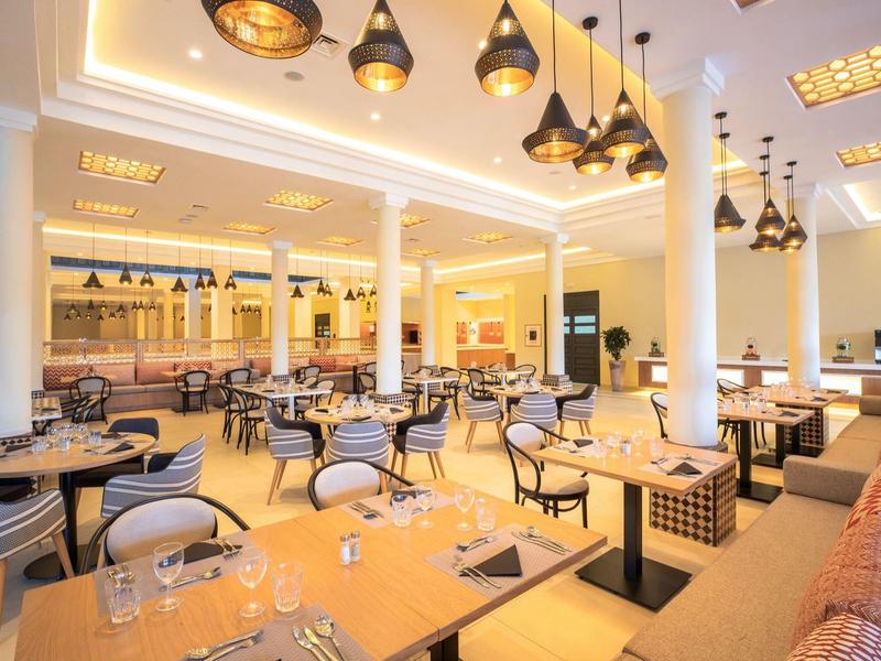 Helles, modernes Restaurant mit runden Holztischen, gepolsterten Stühlen und stilvollen Hängelampen.