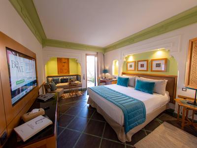 Camera d'hotel luminosa con letto grande, accenti blu e TV a schermo piatto a parete.