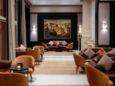 Elegancka strefa lounge hotelowa z pomarańczowymi fotelami, poduszkami i dużym obrazem ściennym.