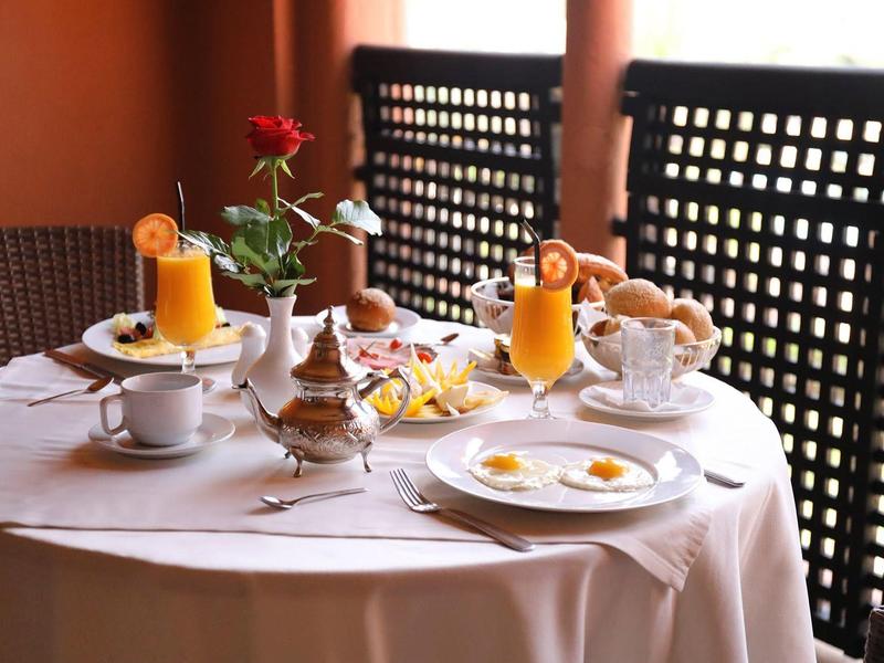 Petit déjeuner élégant avec jus d'orange, thé, pâtisseries et roses sur une table ronde dressée.