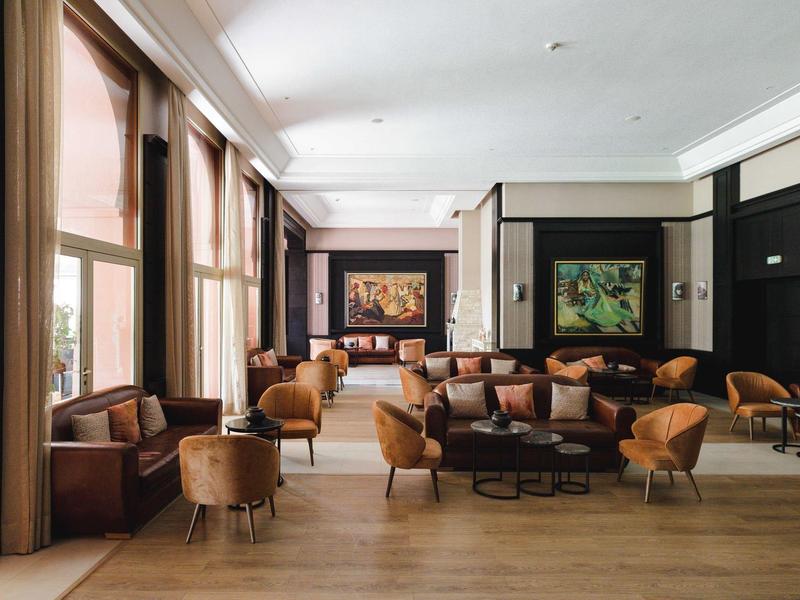 Salon d'hôtel élégant avec fauteuils marron et grandes fenêtres le long du mur.