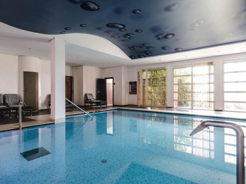 Piscine intérieure avec eau bleue, fenêtres en verre et colonnes blanches dans un hôtel.