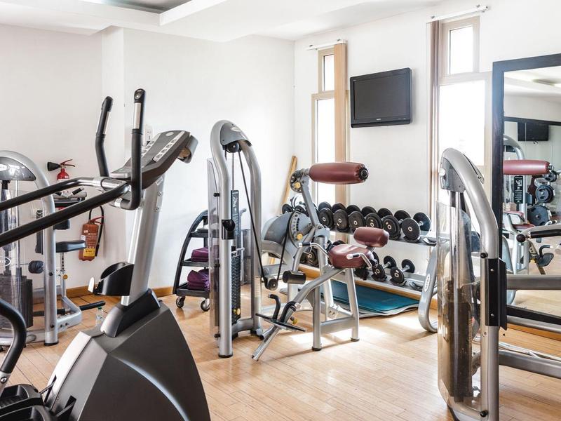 Salle de sport lumineuse avec différentes machines d'exercice et haltères au mur.