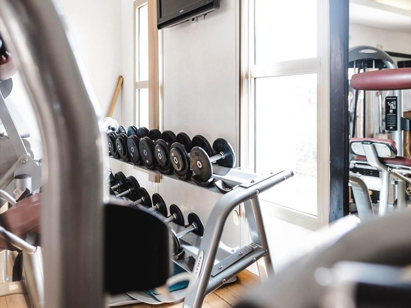 Salle de sport lumineuse avec haltères, miroirs et télévision murale.