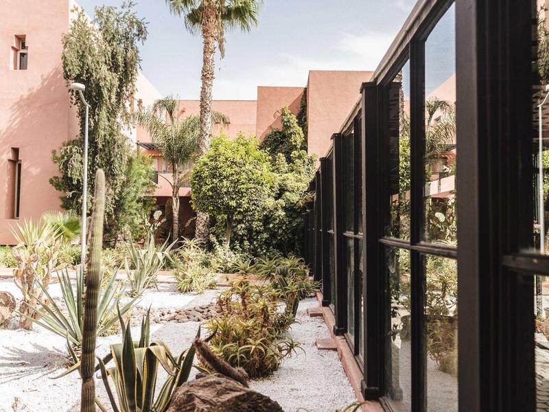 Cour intérieure d'hôtel moderne avec piscine, palmiers et grandes fenêtres le long du bâtiment.