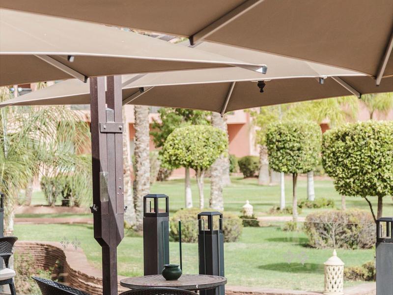 Espace de restauration en plein air avec tables, chaises et grands parasols dans un jardin.