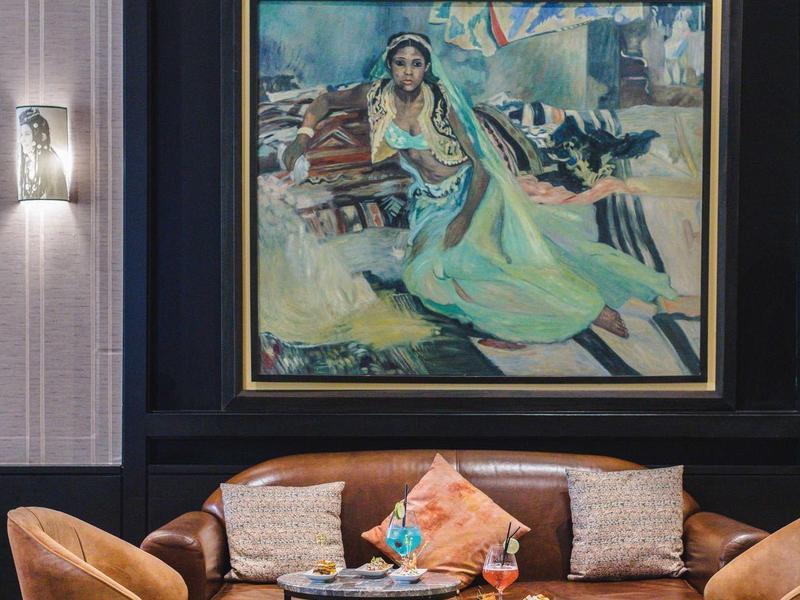 Coin salon élégant avec canapé en cuir, fauteuils et une grande œuvre peinte au mur.