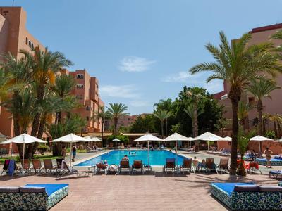 Großer Außenpool mit weißen Sonnenschirmen und Palmen zwischen Hotels.