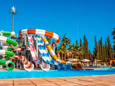 Wasserpark mit bunten Rutschen neben einem Pool und vielen Bäumen im Hintergrund.