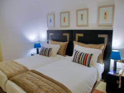 Ein sauber eingerichtetes Doppelzimmer mit zwei Einzelbetten, braunen und weißen Bettdecken und blauen Nachttischlampen.