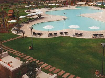 Großer Hotelpool mit Liegestühlen und Schirmen, umgeben von gepflegtem Rasen und Pflanzen.