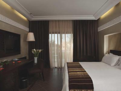 Modernes Hotelzimmer mit großem Bett, Schreibtisch und Balkon hinter Vorhängen.