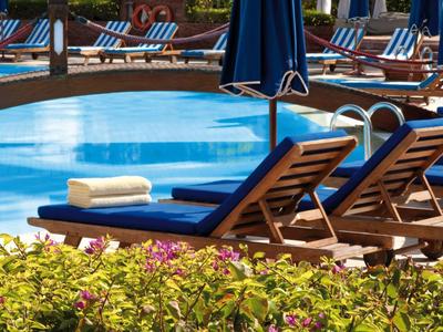 Mehrere Sonnenliegen mit Handtüchern neben einem glatten, blauen Pool, umgeben von Pflanzen.