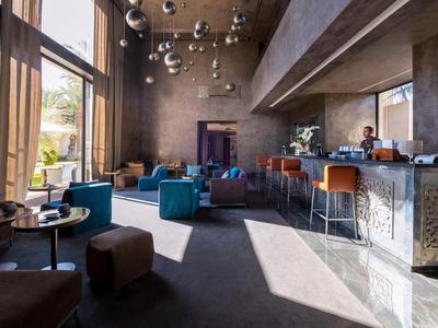 Moderna hall dell'hotel con grandi finestre, poltrone blu e un bar con sgabelli arancioni.