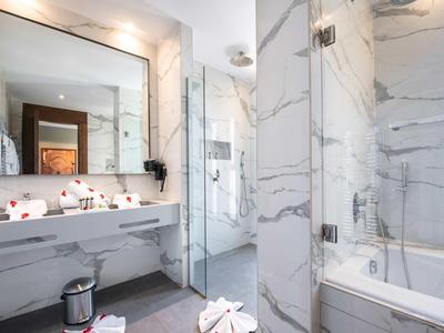Doccia d'hotel moderna con divisorio in vetro, bagno in marmo e lavabo bianco.