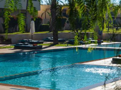 Piscina moderna dell'hotel con palme e ombrelloni alla luce del giorno.