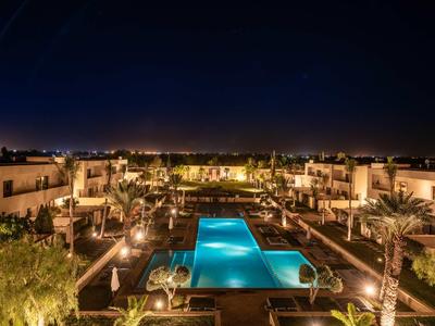 Vista notturna di una piscina d'hotel illuminata circondata da giardini e edifici moderni.
