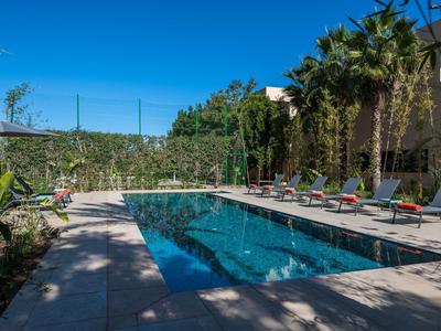 Piscina esterna moderna con lettini e palme in un ambiente da hotel sotto un cielo azzurro.
