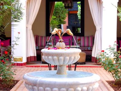Fountain with flowing water in front of a covered seating area with curtains and plants.