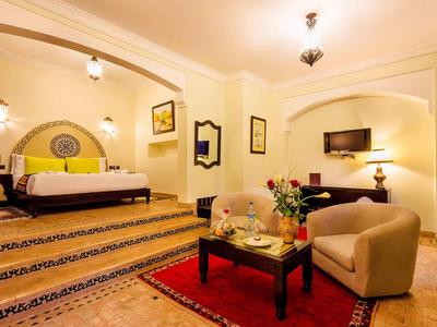 Brightly decorated hotel room with bed, seating area, and TV in warm tones.