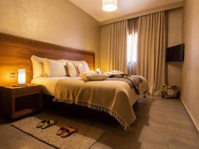 Przytulny pokój hotelowy z dużym łóżkiem podwójnym, lampkami nocnymi i ciepłymi drewnianymi akcentami.