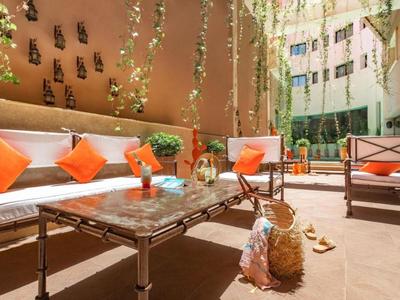 Przytulny taras z sofami, pomarańczowymi poduszkami i wiszącą zielenią na dziedzińcu hotelu.