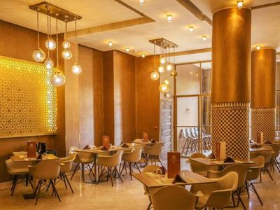 Jasna restauracja hotelowa ze złotymi kolumnami, nowoczesnymi krzesłami i ciepłym oświetleniem.