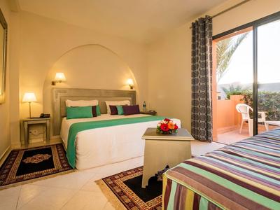 Helles Hotelzimmer mit Doppelbett, Sitzbereich und Blick auf Außenterrasse und Landschaft.
