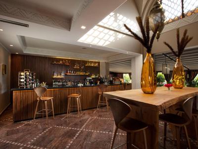 Moderner Hotelbarbereich mit Holztheke, Hockern und dekorativen Vasen auf einem Holztisch.