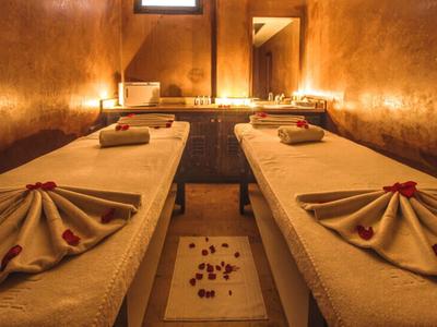 Ein entspannter Spa-Raum mit zwei Behandlungsbetten, warmen Holzwänden und stimmungsvoller Beleuchtung.