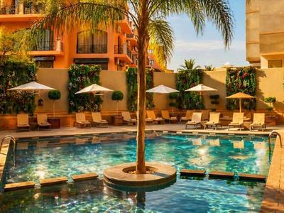 Moderner Hotelpool mit Palmen und Sonnenliegen in sonnigem Ambiente.