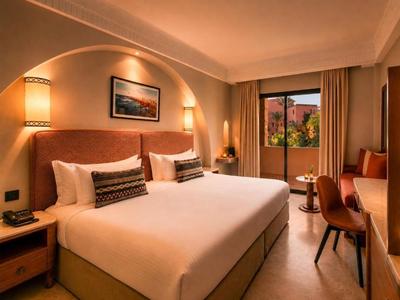 Elegantes Hotelzimmer mit großem Bett, warmem Licht und Balkon mit Blick auf die Natur.